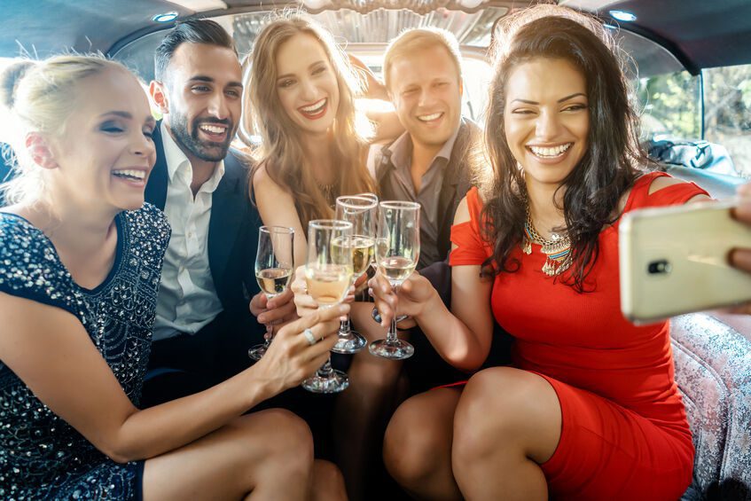 People in the back of a limo, holding champagne glasses and taking a photo together.