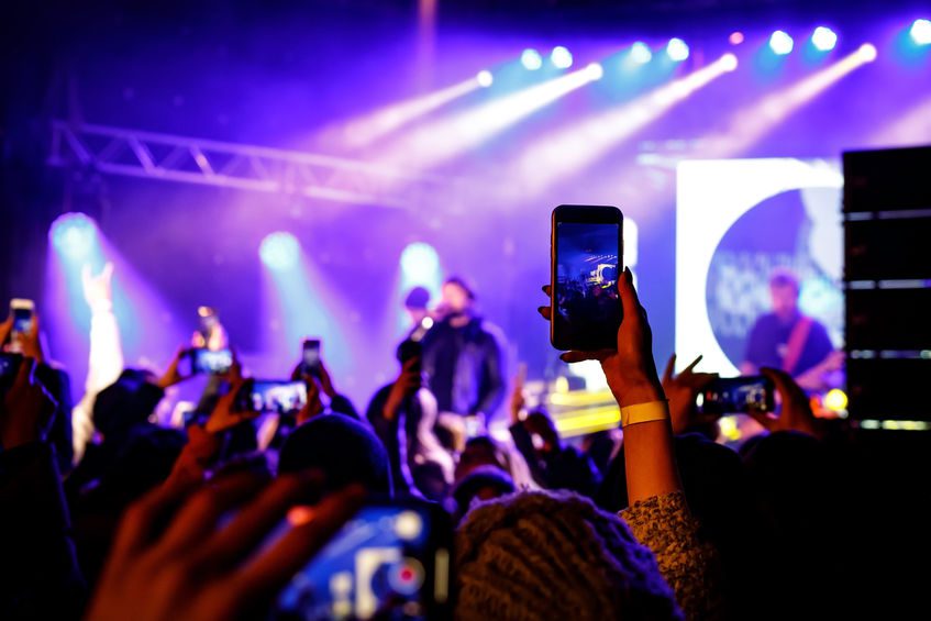 A crowd at a concert with someone recording it on their phone